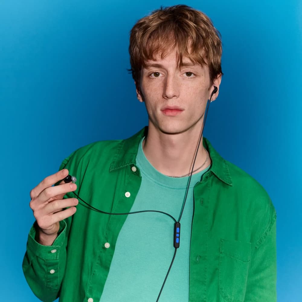 Person wearing black wired Bose earbuds with an inline controller against a blue background.